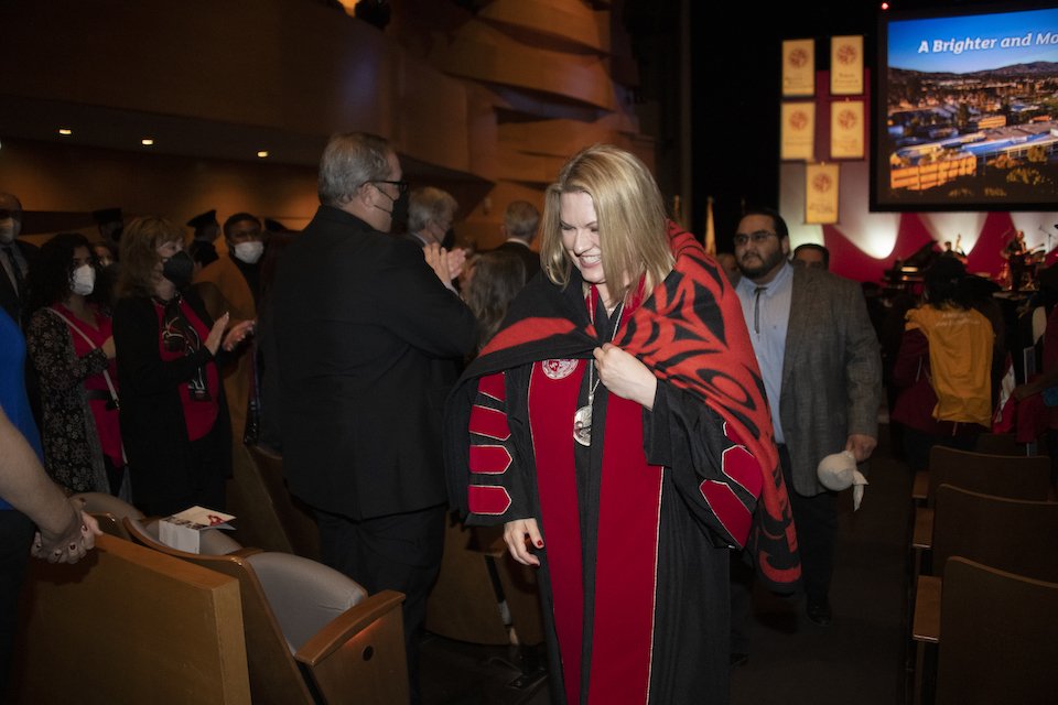 Erika D. Beck in black robe, with colorful Native American blanket on her shoulders walking in aisle