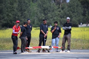 Students stand by an airplane model in an open field.