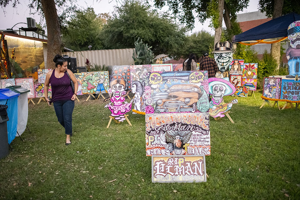 A woman looks at more than a dozen paintings on canvas and posters, as well as ofrendas, set up on the lawn outside the Chicano House.