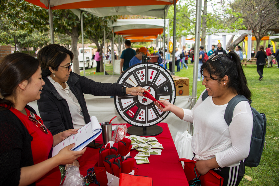 Woman spinning a wheel to win a prize at a table with prizes from CSUN Dining.