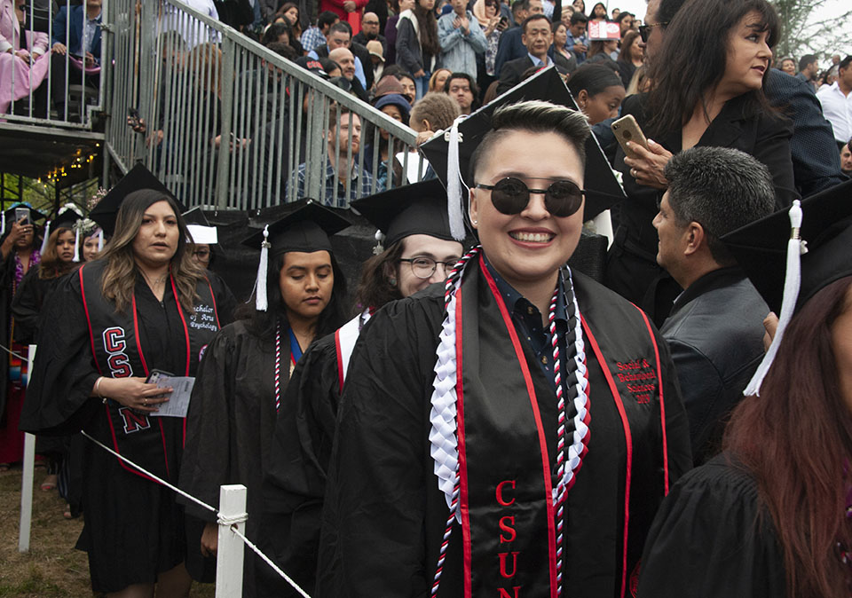 smiling college graduate is wearing black round sunglasses and arriving at a graduation ceremony.