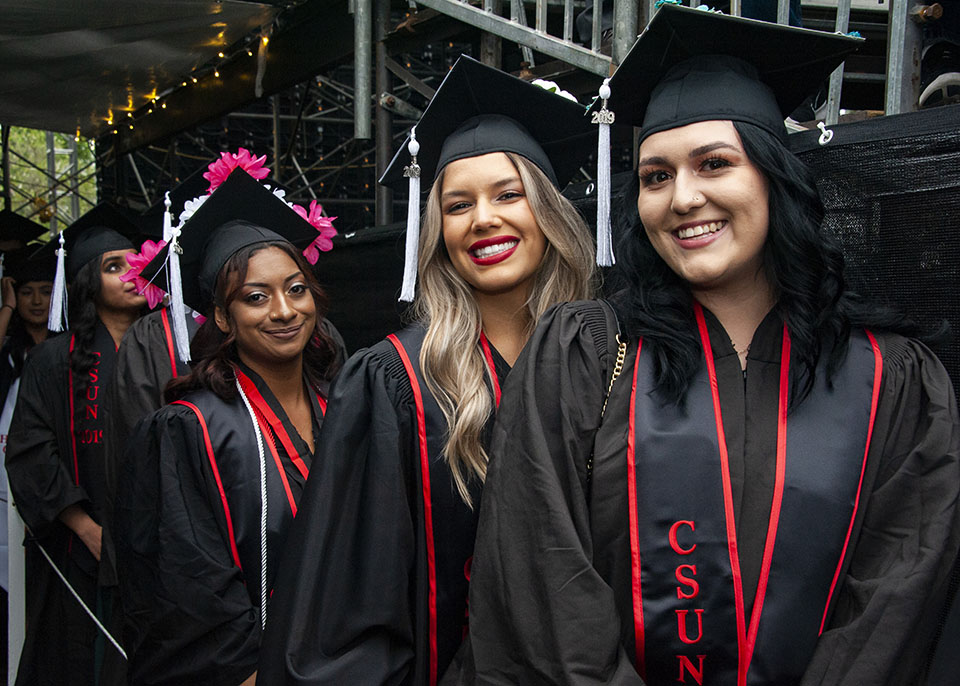 Three college graduates smile together as they arrive at a graduation ceremony.