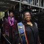 Smiling college student is wearing a navy blue sash that says 'EOP 50 Years RSP' and arriving to a graduation ceremony.