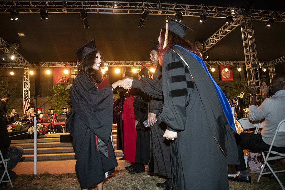 Faculty members shake hands with a graduate in cap and gown, as she walks down from the Commencement in front of the University Library.
