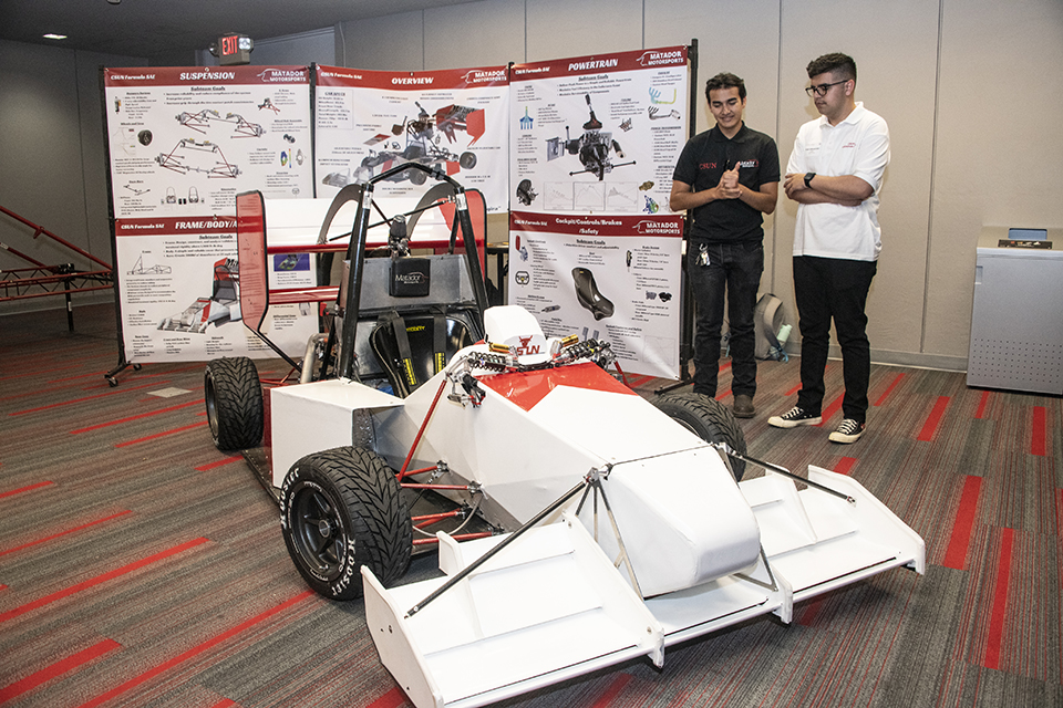 The completed car stands in front of detailed posters with the specs of the car.