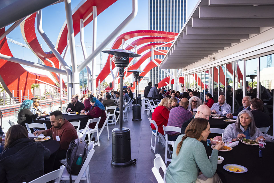 People sit at tables with the distinctive metal swirls of the Petersen Automotive Museum above them.