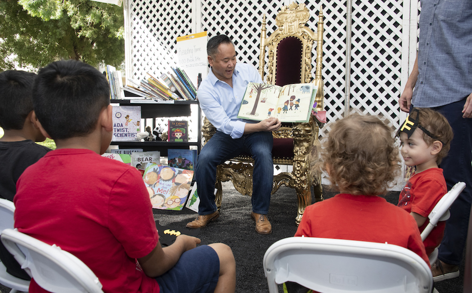 Lee sits in front of children with open book