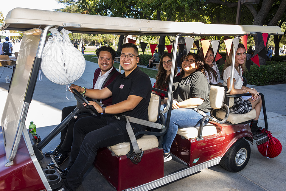 Golf car with two students seated in front and students seated in the back.