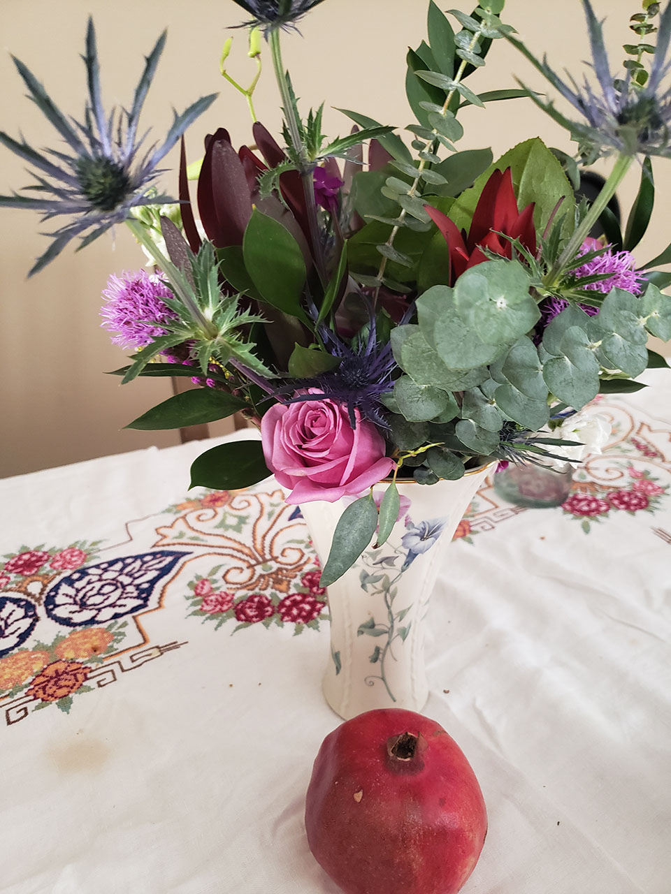 A colorful bouquet of flowers in a vase, with a red pomegranate placed in front.