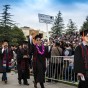 Graduates in caps, gowns and floral leis walk in procession.