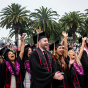 Graduates in caps and gowns and colorful leis cheer in the audience
