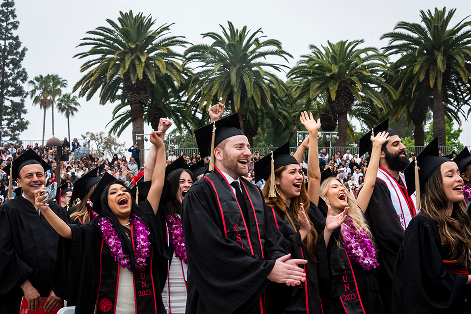 Graduates in caps and gowns and colorful leis cheer in the audience