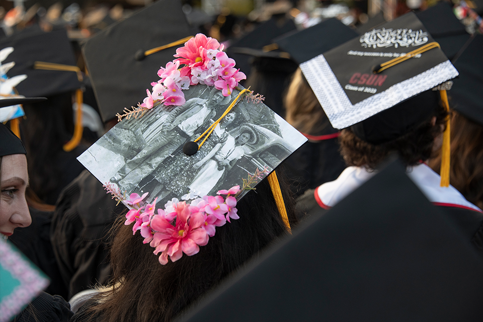 A mortarboard is decorated with pink flowers along with an old-time black and white photograph of a man and woman