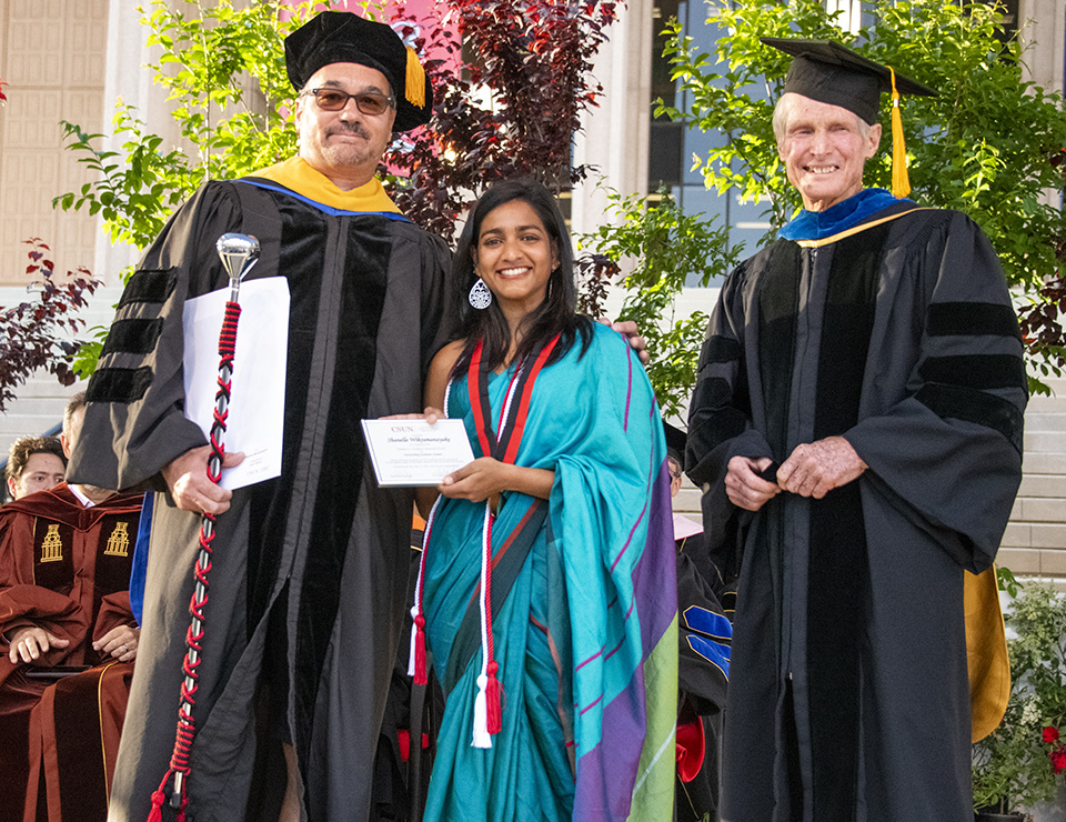 Graduating master's student Shanelle Wikramanayake, in a blue-and-purple sari, holds an award certificate, standing between two faculty members.