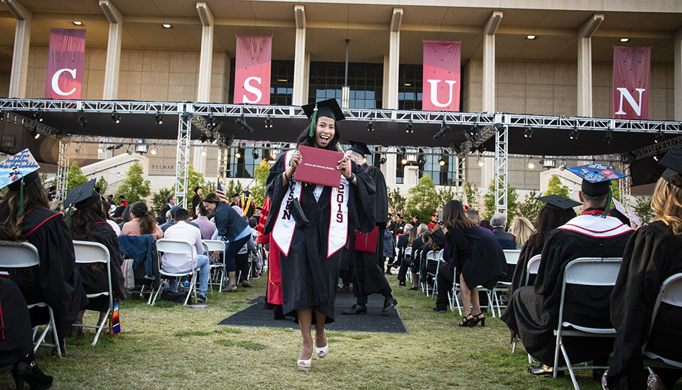 A CSUN graduate proudly displays her diploma as she crosses an aisle at CSUN commencement.