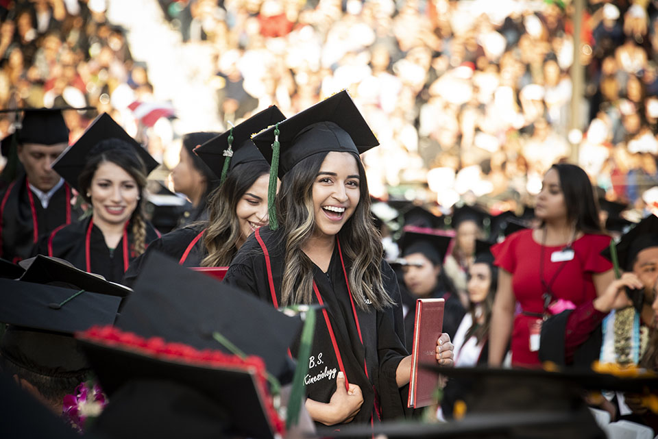 A female kinesiology student carries her diploma at CSUN commencement.