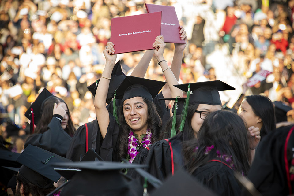 A female student hoists her diploma in the air.