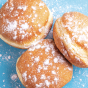 Three fluffy sufganiyot (jelly donuts), dusted with powdered sugar, on a blue table surface.