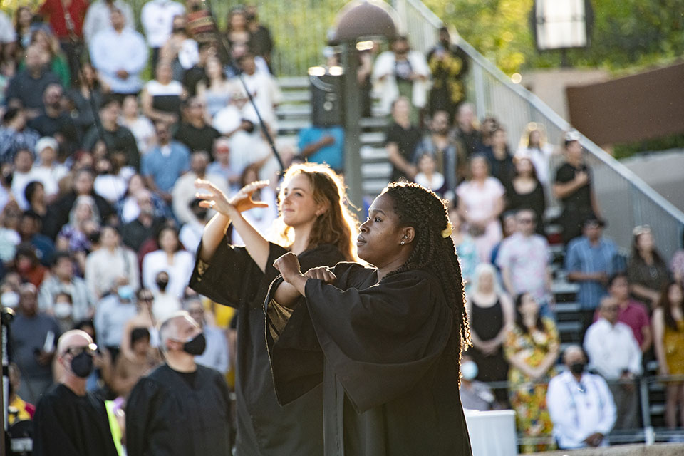 Two CSUN graduates in black Commencement gowns perform the National Anthem in American Sign Language, at Honors Convocation 2022.