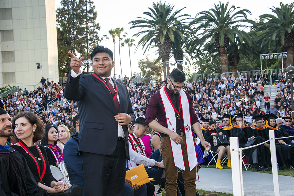 a student wearing a medal points to the crowd at a graduation ceremony.