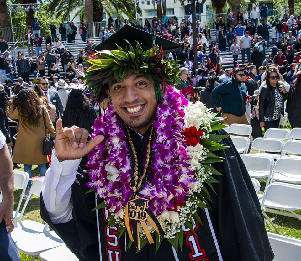 A CSUN student is heavily decorated with flowers around his neck and cap.