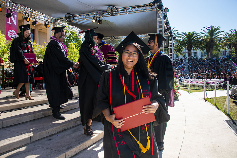 A CSUN graduate proudly exits the commencement stage with her diploma.