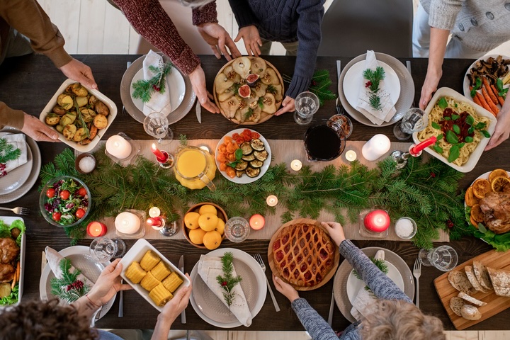 Top view of hands of family members holding plates with homemade food and desserts while serving festive table before Christmas dinner. Credit: shironosov via IStock
