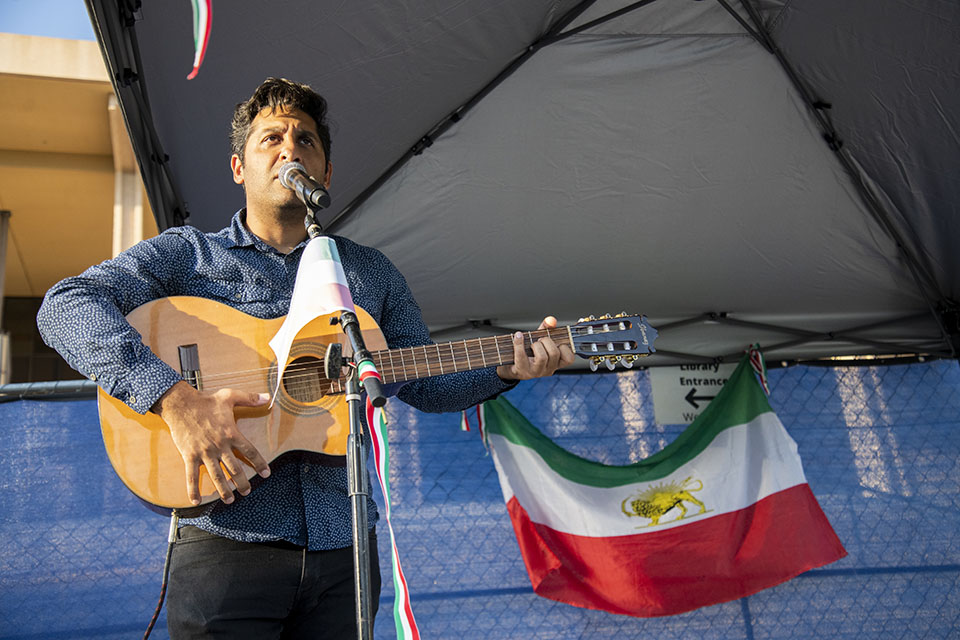 Close up of man singing with guitar. Iranian flag is in the background.