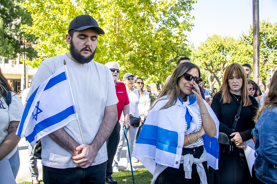 Two students stand together, one carrying a blue and white Israeli flag, the other student wearing a large Israeli flag around her shoulders.