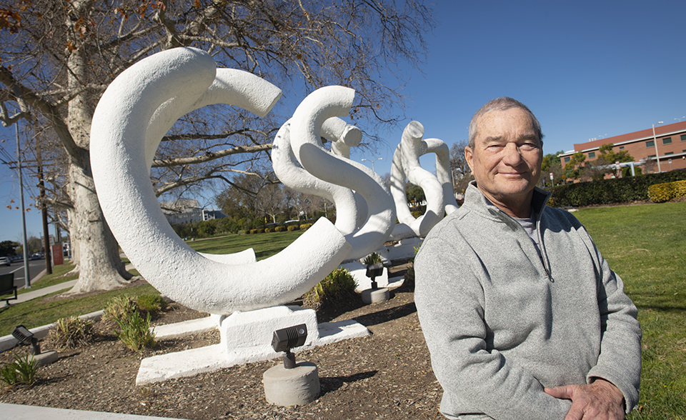 John Banks sits in front of a large outdoor sculpture that spells out 