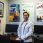 Justin Aragon stands in front of posters showing services provided by the Veterans Resource Center