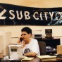 Louis Posen at an old desktop computer with a Sub City banner in back of him.