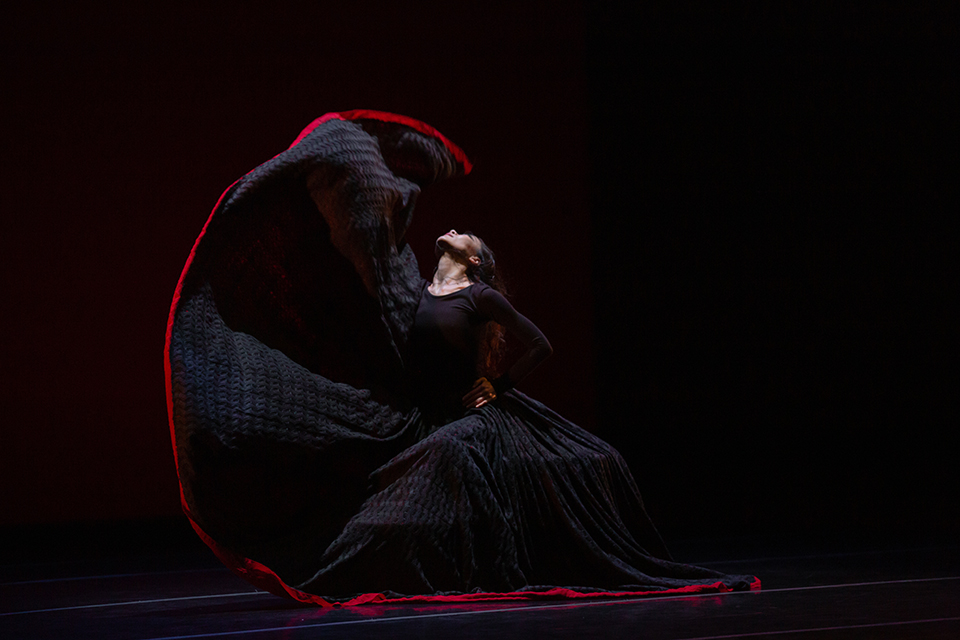 A dancer from the Martha Graham Dance Company creates a striking silhouette with her black dress with a red line at the bottom.