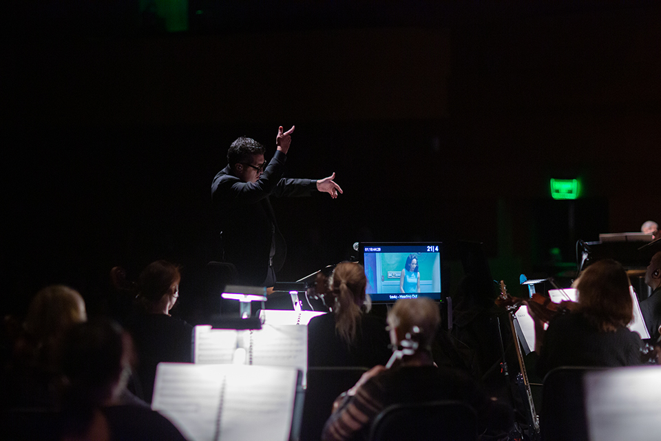 Cheche Alara conducts New West Symphony while a scene from 