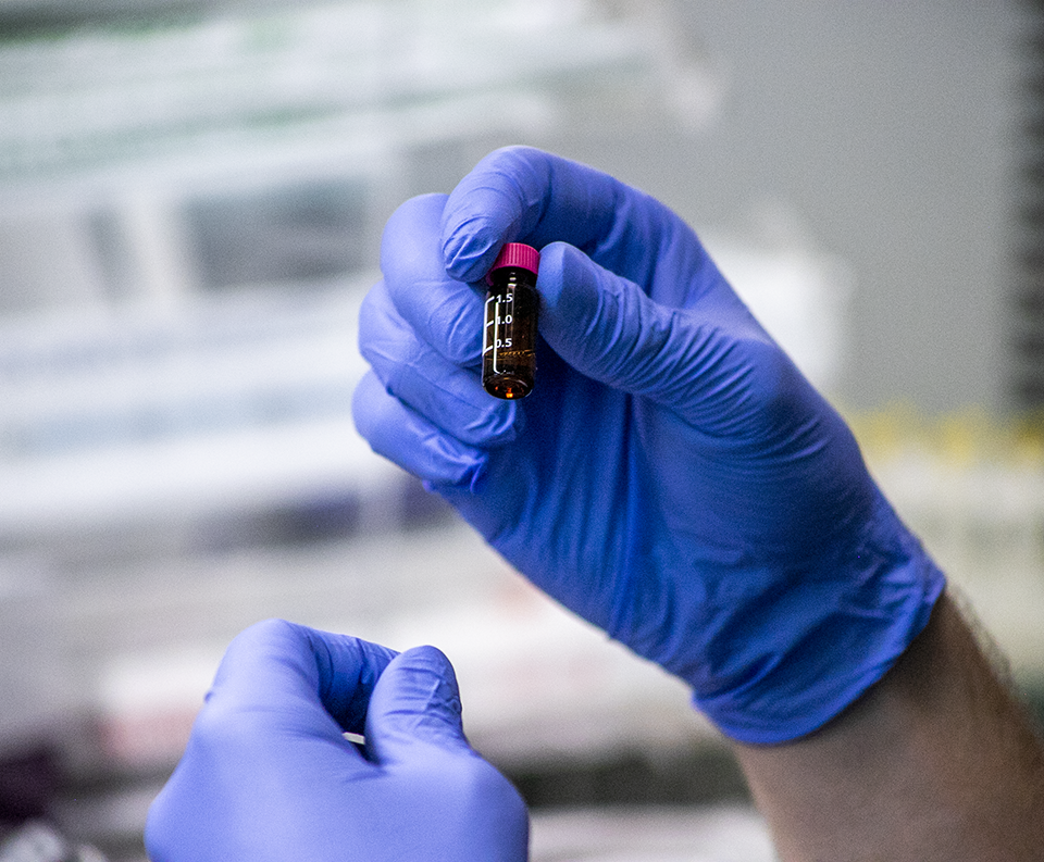 Gloved hands hold a vial of blood in a cancer research lab.