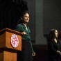 Lauren Ridloff stands smiling on stage by podium with CSUN seal. An American Sign Language translator, dressed in black stands in the background.