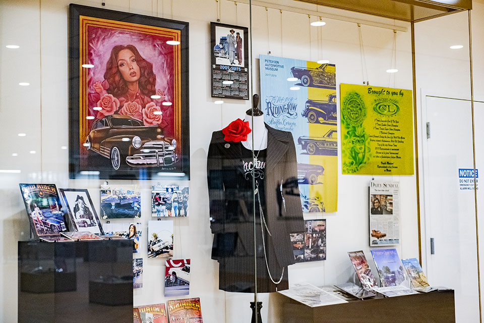 Glass fronted exhibit case with posters and flyers and a women's black pinstripe suit featured.