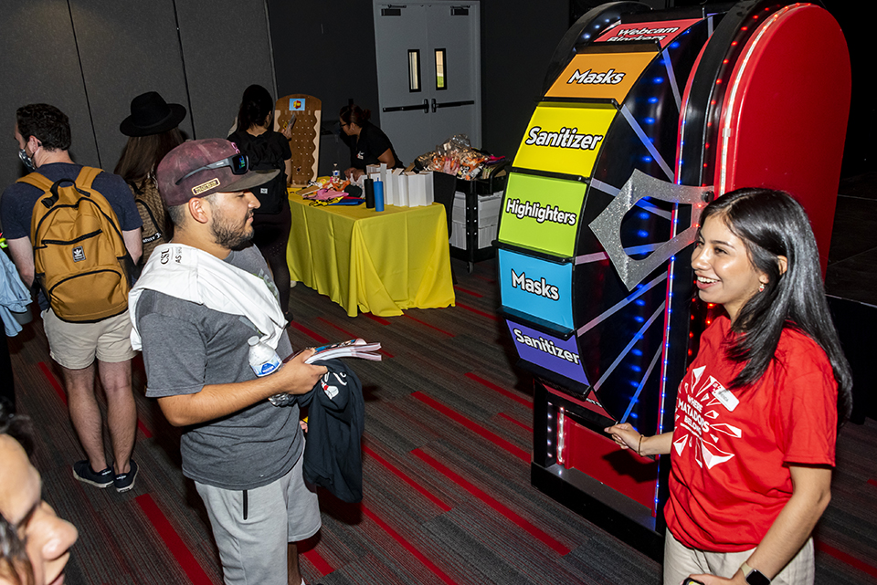 Student stands in front of Spin the Wheel game with student from Associated Students.
