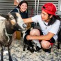 Two CSUN students crouch down to pet a larger goat and a baby goat (a kid) inside a small petting zoo pen, at the University Student Union.