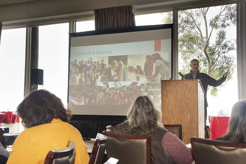 Matt Cahn stands at a podium in front of a screen, speaking before an audience of faculty.