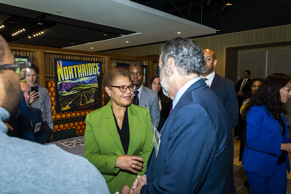 Los Angeles Mayor Karen Bass shakes hands with a man in a blue suit as she walks through the Orchard Conference Center Lobby.