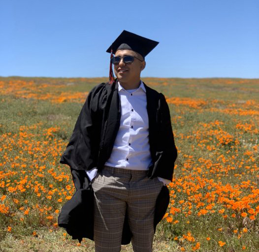A CSUN student poses in graduation gear in front of a field of orange poppies.