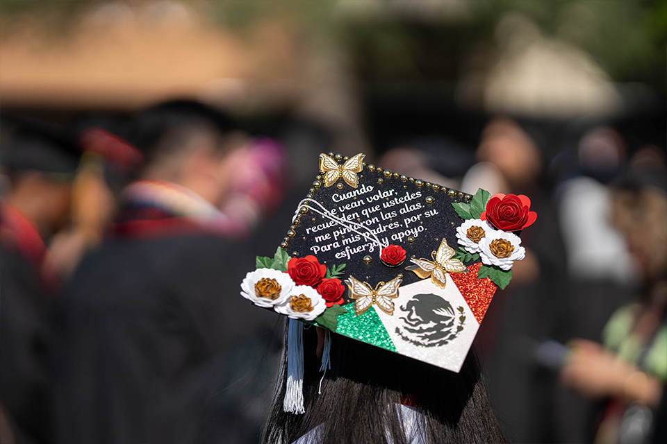 Mortarboard features red, green and white stripes with flowers and message in Spanish.