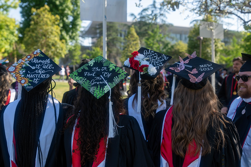 Four graduates stand together with their back to the camera showing their decorated mortarboards