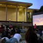People sit on the lawn in front of the CSUN Library as a movie plays on a giant screen in the distance.