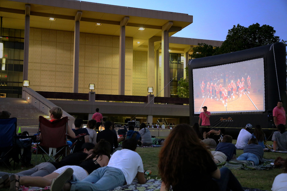 People sit on the lawn in front of the CSUN Library as a movie plays on a giant screen in the distance.