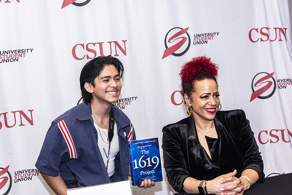 Student sits with Nikole Hannah-Jones at table. Student holds up book and both smile for the camera.