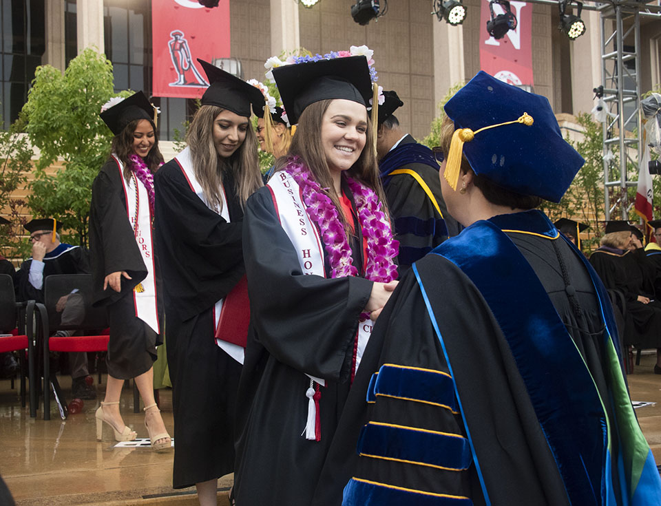 A college graduate smiles and shakes a faculty member's hand on a graduation stage.