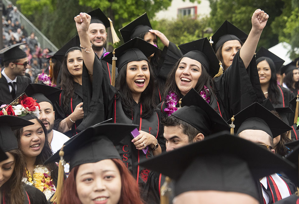College graduates raise their fists and smile during the 2019 CSUN commencement ceremony.