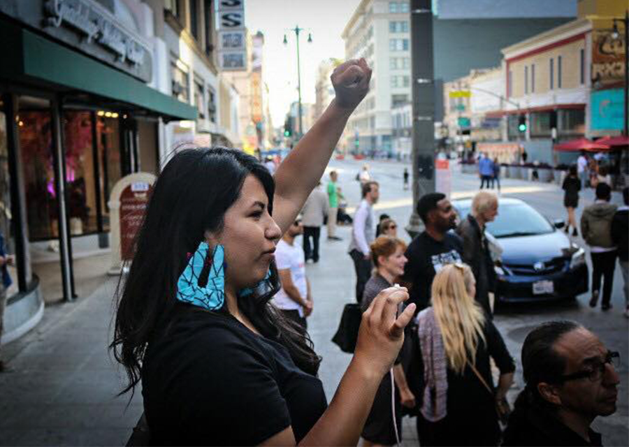 Noemi Tungüi raises a fist in the air as she stands on a street in Los Angeles.